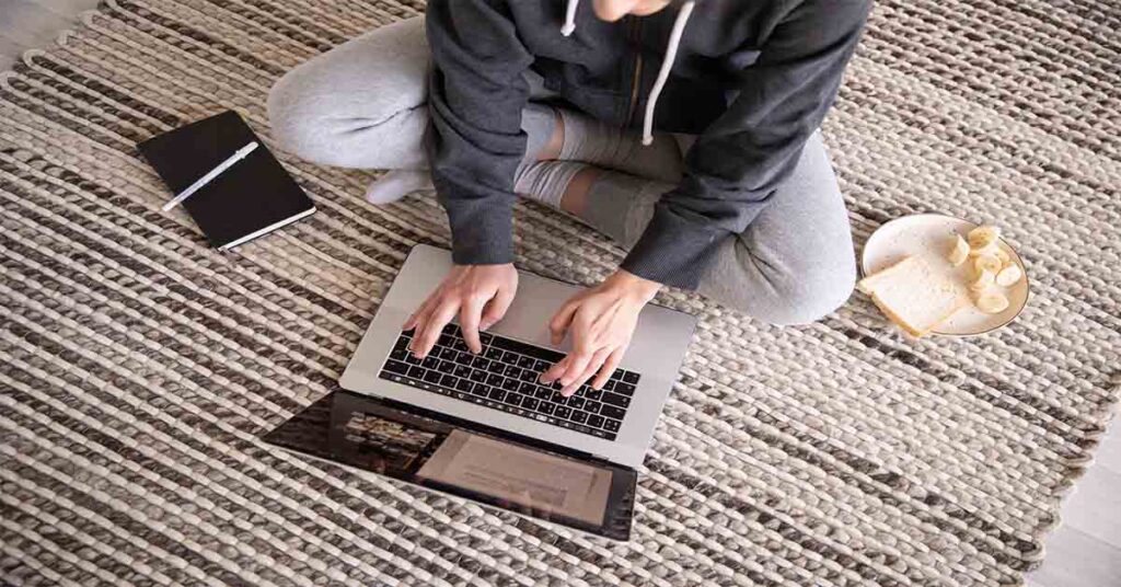 Girl sitting on a carpet with laptop and foods, pc on carpet